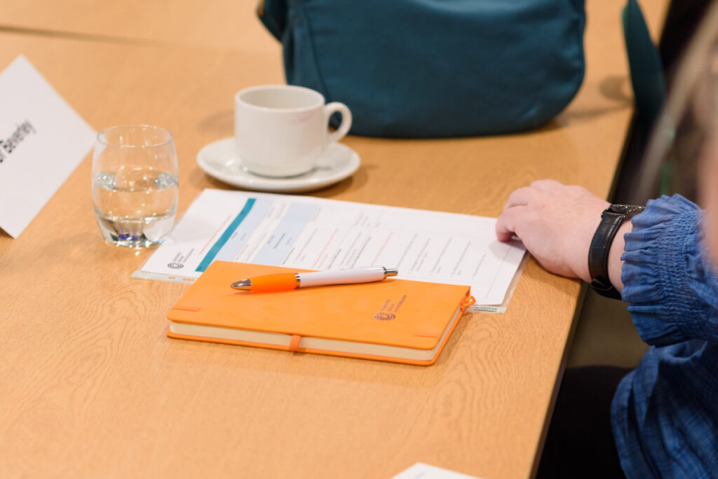 Orange notebook sits on a table next to a printed agenda. A woman's hand rests against both.